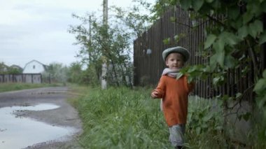 Komik çocuklar, şapkalı ve lastik çizmeli bebek dışarıda oynamayı ağaçlardan yaprakları koparmayı ve onları su birikintisine atmayı seviyor.