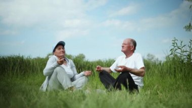 Yaşlılıkta sağlıklı bir yaşam tarzı, sportif yaşam tarzını seven yaşlı bir çift dışarıda yoga minderinde yeşil bir çimenlikte fiziksel egzersiz yapıyor.