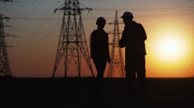 Koruyucu miğfer takan mühendisler, elektrik ve silüet tedarik etmek için yeni bir elektrik hattı inşa edilmesi konusunu tartışırken elleriyle konuşuyorlar.