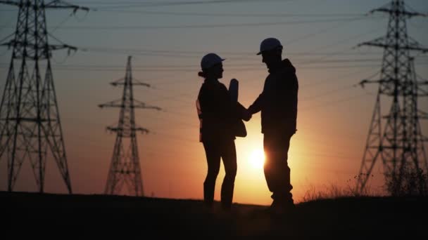 Energy efficiency concept, a team of engineers in protective helmets a man and a woman discussing high-voltage poles, silhouette — Stock Video
