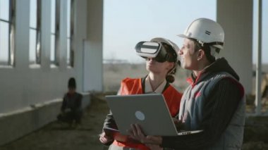 Gelişmiş teknolojiler, uzman mühendisler ve koruyucu miğfer takan bir mimar VR cihazlı kadın yeni bir hangar projesinin dikey gerçekliğini keşfediyor.