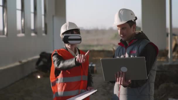 Presentación moderna, ingeniero femenino y masculino en gafas de realidad virtual y portátil en la mano en cascos de protección discutir nuevo proyecto de construcción — Vídeo de stock