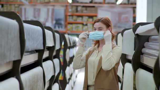 Chica comprador elegir fondo de pantalla en la ferretería después de la pandemia, mujer sonriente joven se pone una máscara médica protectora en una tienda departamental — Vídeo de stock