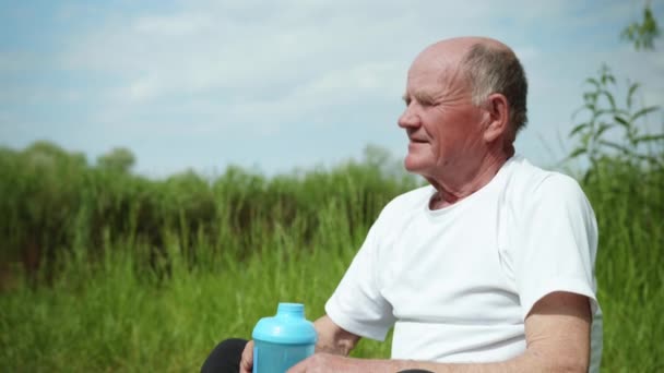 Пожилой красивый мужчина наслаждается жизнью и пьет чистую здоровую воду из спортивной бутылки после занятий спортом — стоковое видео
