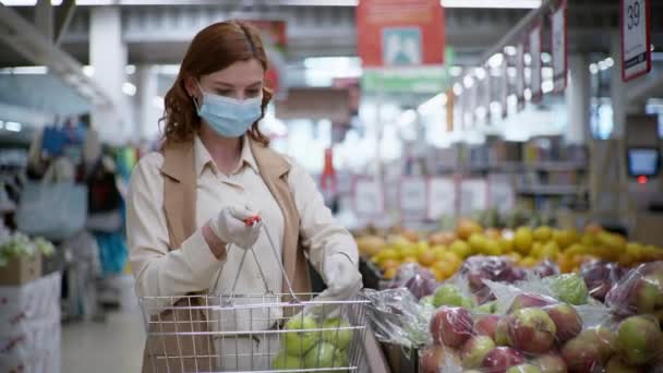 Protección contra el virus, retrato de una mujer con máscara médica y guantes goteando fruta en un supermercado — Vídeos de Stock