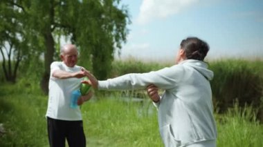 Yaşam tarzı, dışarıda çalışan yaşlı bir çift, yaşlı bir adam spor veya meditasyon yaptıktan sonra karısına bir şişe su verir.