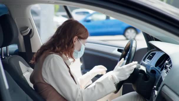 戴着医疗面罩和手套的年轻女司机上车，给方向盘和手套消毒 — 图库视频影像