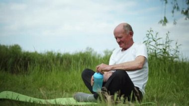Sağlıklı beslenen, yaşlı bir adam sağlıklı bir yaşam sürüyor ve yoga veya meditasyondan sonra spor şişesinde temiz su içiyor.