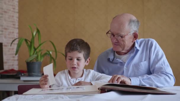 Сімейні спогади, маленька весела дитина зі своїм дідусем, перегляд фотоальбому — стокове відео