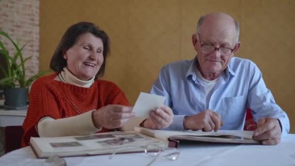 Семейные воспоминания, любящая пожилая пара, сохранившая нежные чувства друг к другу, вспоминают счастливые моменты счастливой жизни, глядя на свой дорогой семейный фотоальбом — стоковое видео