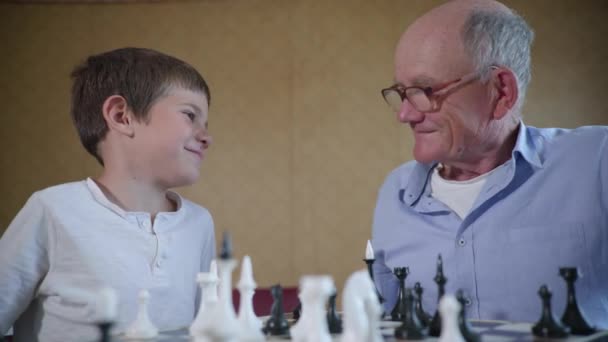 Großvater hat Spaß mit seinem geliebten attraktiven Enkel, der mit ihm am Familienwochenende lehrreiche Schachbrettspiele spielt — Stockvideo