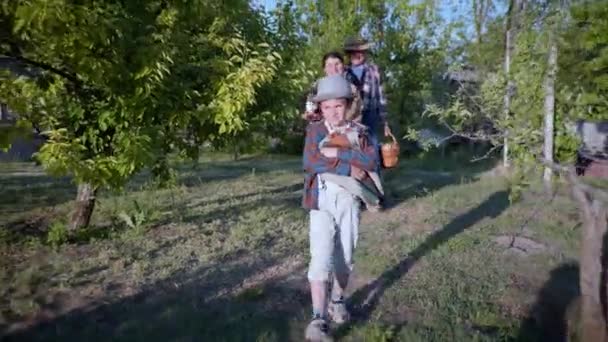 Familjesemester, glada barnbarn med morföräldrar i halmhatt och en picknickkorg i händerna gående längs tropikerna bland träden — Stockvideo