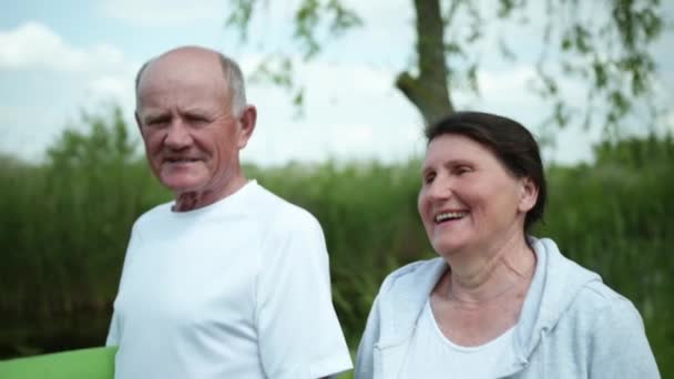 Улыбающиеся старые женатые пара пожилых мужчин и женщин с ковриком для йоги или медитацией в руках мило болтают между собой — стоковое видео