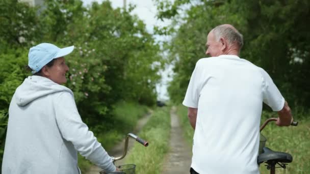 Pensionati allegri, un vecchio e una donna anziana divertirsi a piedi con le biciclette, nonni carino felicemente chiacchierare in bicicletta — Video Stock