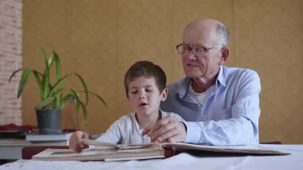 Grand-père âgé avec des lunettes pour la vision mignon avec le garçon profiter de souvenirs heureux raconter des souvenirs des années passées et regarder l'album photo de famille — Video