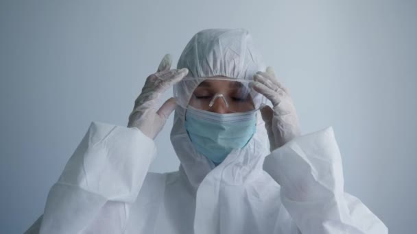 Feliz doctora en traje protector disfrutando del final de la jornada laboral durante la pandemia debido al coronavirus sobre fondo blanco — Vídeo de stock