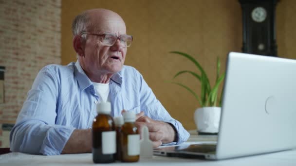 Medicina a distancia, un anciano de edad avanzada con gafas para la visión consulta a un médico en línea a través de la comunicación de vídeo en un ordenador portátil utilizando la tecnología moderna dice que sus síntomas de la enfermedad — Vídeos de Stock