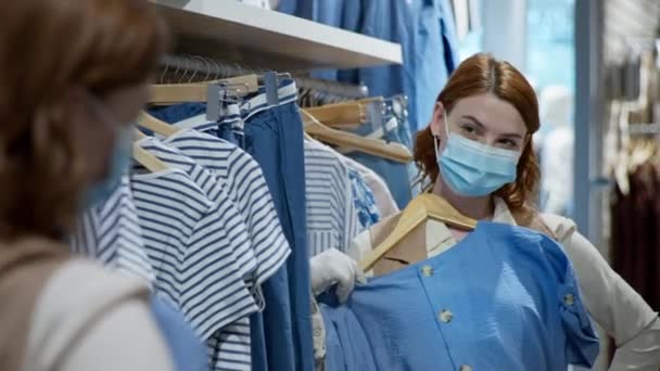 Chica en máscara médica y guantes elige ropa nueva en el campo de compras la eliminación de carnitina y la apertura de la tienda al por menor — Vídeos de Stock