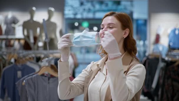 Compra en coronavirus, feliz cliente femenino en guantes médicos poniéndose mascarilla para proteger contra virus e infecciones en tienda de ropa — Vídeo de stock