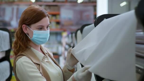 Quarantaine reparaties, een jonge vrouw koper in een beschermend masker en handschoenen selecteert het behang om het ontwerp van haar appartement bij te werken tijdens isolatie — Stockvideo