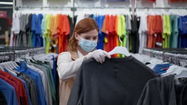 Shopping Quarantäne, eine zufriedene Kundin mit medizinischen Masken und Handschuhen wählt Kleidung, nachdem die Quarantäne während einer Pandemie entfernt wird. — Stockvideo