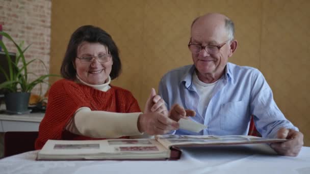 Семейные воспоминания, веселая супружеская пара пожилой мужчина и женщина наслаждаются воспоминаниями листая старые семейные альбомы с фотографиями — стоковое видео