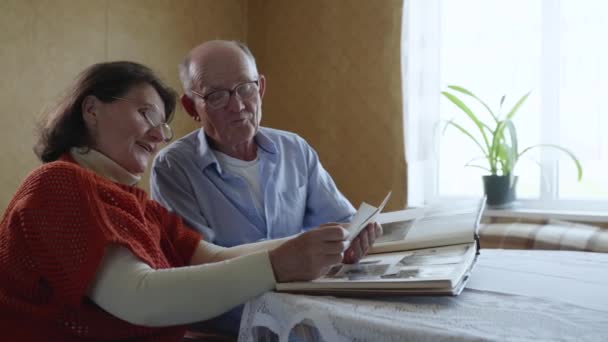 Vreugdevol getrouwd stel oude mannen en vrouwen verheugen zich en lachen genieten van familieherinneringen kijken naar foto 's in fotoalbum — Stockvideo