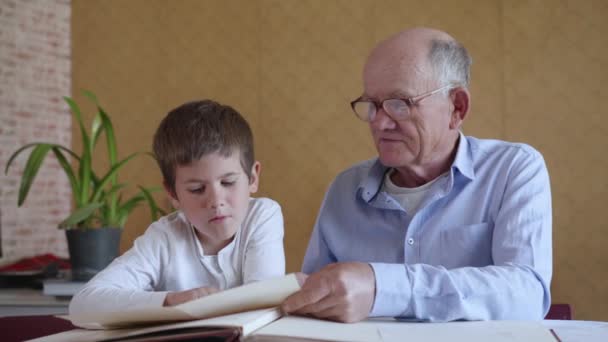 Vieux grand-père dans des lunettes pour la vue avec son petit-fils sympathique profiter souvenirs souvenir regarder un album photo de famille — Video