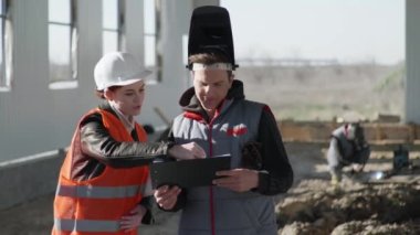Miğferdeki kadın mühendisler inşaat sırasında koruyucu giysi ve kask yapımında uzman bir kaynakçıyla görüşüyor.