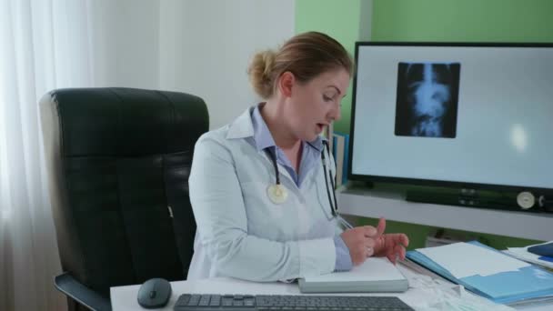 Medico online, terapista femminile consulta con collegamento video e parla delle cause della malattia mentre siede a tavola in sala medica — Video Stock