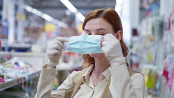 Minorista, chica bonita comprador en guantes pone una máscara en su cara para proteger contra coronavirus mientras que las compras en ropa de los niños — Vídeos de Stock