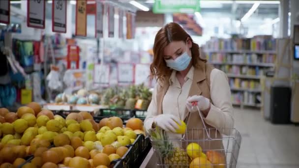 Zakup produktów dla koronawirusa, młodej gospodyni domowej w masce i rękawiczek z koszykiem na zakupy w celu ochrony przed wirusami kupuje produkty w supermarkecie podczas pandemii — Wideo stockowe