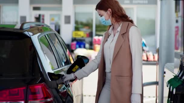 Serviço de carro, uma jovem mulher um motorista com uma máscara protetora e luvas alimenta seu carro em um posto de gasolina durante o isolamento e uma pandemia — Vídeo de Stock