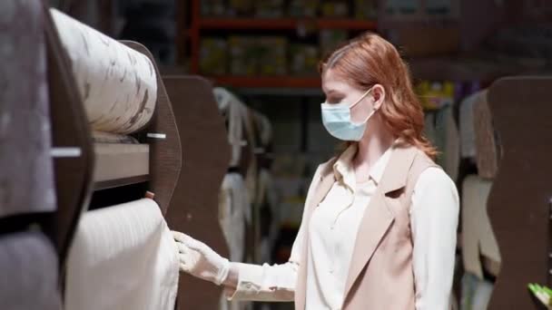 Mujer joven en una máscara médica y guantes para la protección contra el coronavirus elegirá nuevo fondo de pantalla para la renovación del apartamento — Vídeo de stock