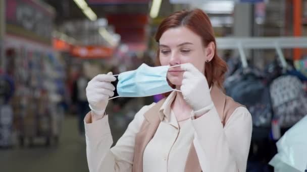 Cliente femenino que usa una máscara y guantes mientras compra en cuarentena debido a un coronavirus en la tienda minorista en medio de una multitud de personas — Vídeo de stock
