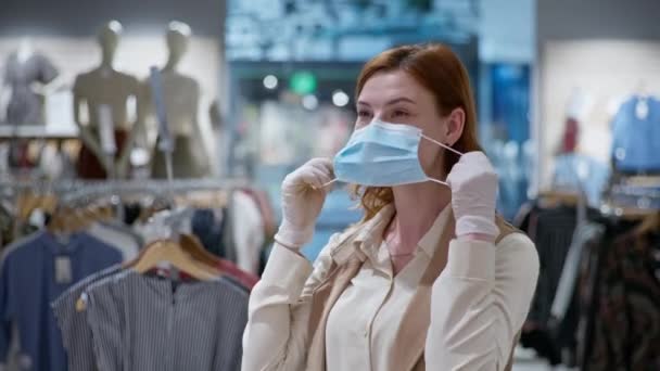 Protección contra el virus, retrato de una chica sonriente con guantes médicos poniendo máscara en su cara en la tienda de ropa — Vídeo de stock