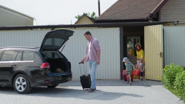 Rodinný výlet, rodiče se svými malými veselými mužskými dětmi jet na dovolenou a opustit dům s kufry nakládat zavazadla — Stock video