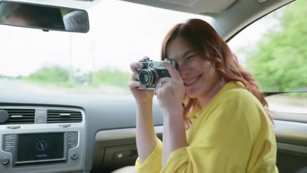 Cestování, radostná atraktivní žena baví a fotografování s retro kamerou při cestování autem o letním víkendu — Stock video
