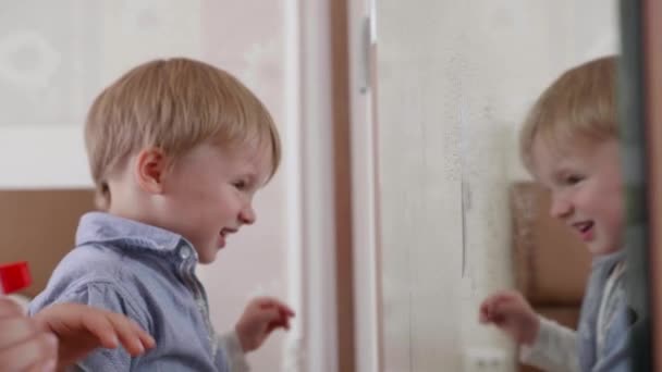 Casa de limpieza, lindos niños pequeños rociar detergente de limpieza en el espejo y lavarlo con un paño de limpieza en la habitación de la casa — Vídeos de Stock