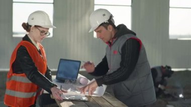 Koruyucu miğferlerdeki mühendisler, kaynak kirişlerinin arkaplanındaki çizimlere göre yeni binayı tartıştılar