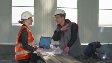 Erkek ve kadın mühendisler, çizimlere göre tezgahın üzerinde dururken düzeltmeler yaparak yeni bir projeyi tartışıyorlar.