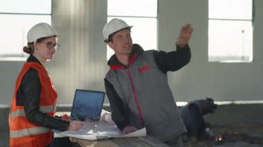 Endüstriyel, koruyucu miğferli mühendis ve teknisyenler bir proje ve çizimler üzerinde çalışıyorlar.
