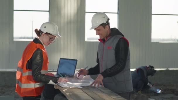 Mužští a ženští stavební inženýři diskutují o novém projektu podle výkresů na pozadí jisker ze svařování — Stock video
