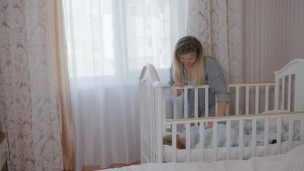 Турбота про дітей молода любляча мати м'яко погладжує свою маленьку улюблену дитину чоловічої статі, яка спить у ліжечку — стокове відео
