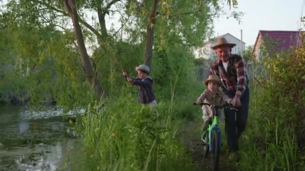 Recreación al aire libre, feliz abuelo atractivo ciclismo su encantador nieto fondo de niño pescador con caña de pescar en sus manos — Vídeos de Stock