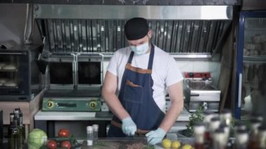 Restoran işi, tıbbi maskeli erkek şef önlem alıyor ve sulu et hazırlıyor. Mutfakta bir hamburger için bir madalyon.