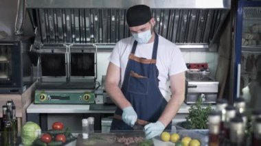 Küçük işletme, tıbbi maske takan, virüs ve enfeksiyondan korunmak için profesyonel şef ve eldivenler fast food kafede hamburgerlere taze et köftesi hazırlıyor.