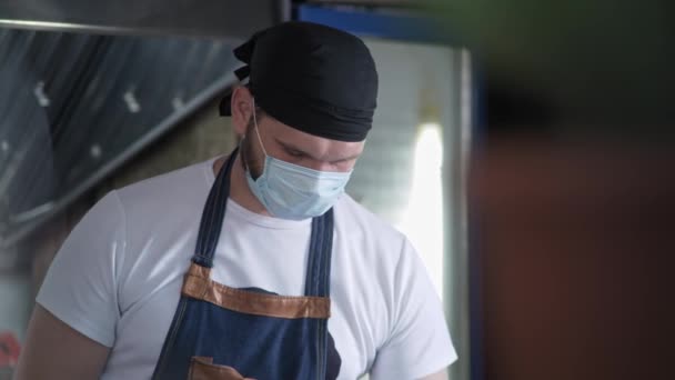 Kök, attraktiv manlig kock i uniform och medicinsk mask förbereder kött i professionell snabbmat restaurang kök — Stockvideo
