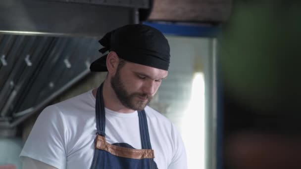 Cocinero masculino en uniforme prepara comida para los visitantes en un café de comida rápida sobre un fondo de parrilla — Vídeos de Stock