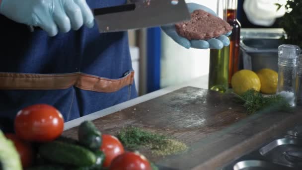 Profesionální kuchař s rukavicemi kuchař dělá masové medailony pro hamburgery s nožem na maso na řezací desce pozadí zeleniny, místní výrobce — Stock video
